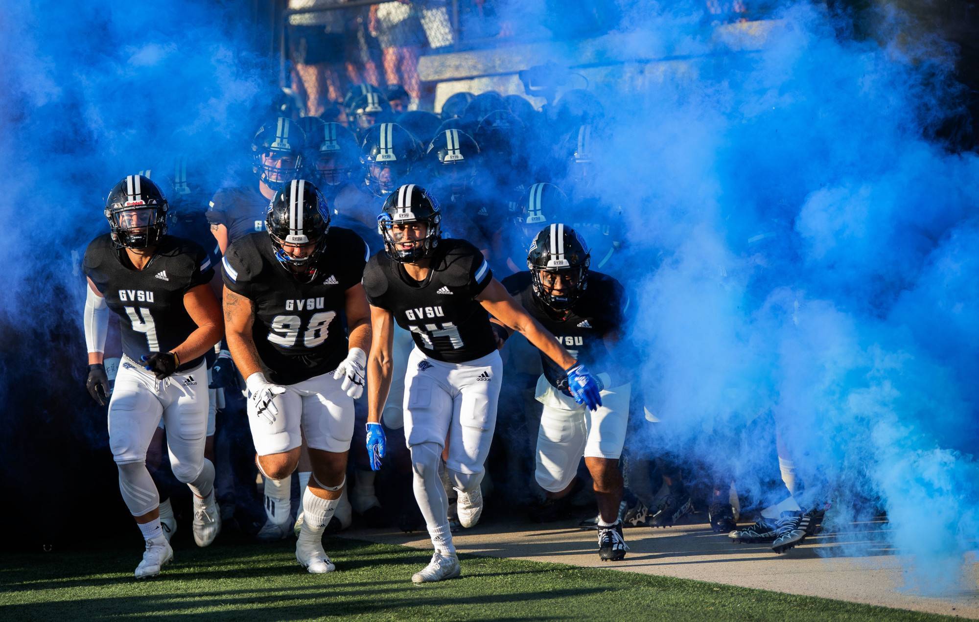 Football players run onto the field with blue smoke